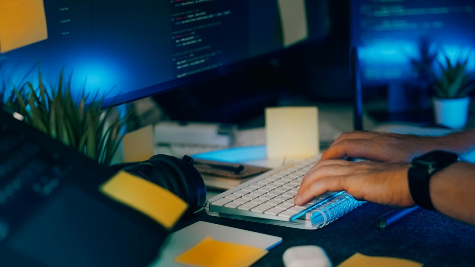 Manos escribiendo en un teclado frente a pantallas con código